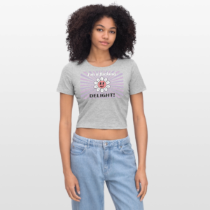 Model draagt een grijs gemêleerde cropped top met "I'm a fucking Delight!" een vrolijke retro bloem in roze en wit en paarse retro zonnestralen op de achtergrond, boven lichtblauwe denim jeans.