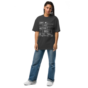 Vrouw draagt oversized statement t-shirt van 100% katoen met tekst "Don't be just another brick in the wall" in antraciet met bakstenen muur print, gecombineerd met wijde spijkerbroek voor een relaxte streetwear-look.